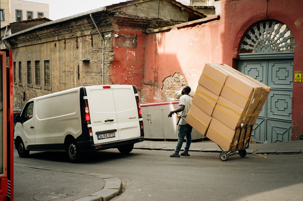 A mover pulling a cart stacked with boxes beside a van